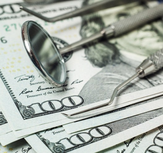 A close-up of dental tools stacked on top of dollar bills