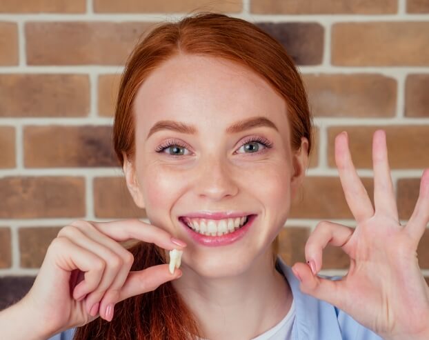 Woman smiling and holding an extracted tooth