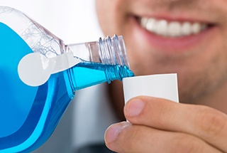person pouring blue mouthwash into a small cup 