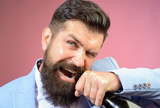 bearded man opening a glass bottle with his teeth 