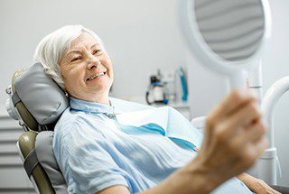 elderly woman admiring her smile in a hand mirror