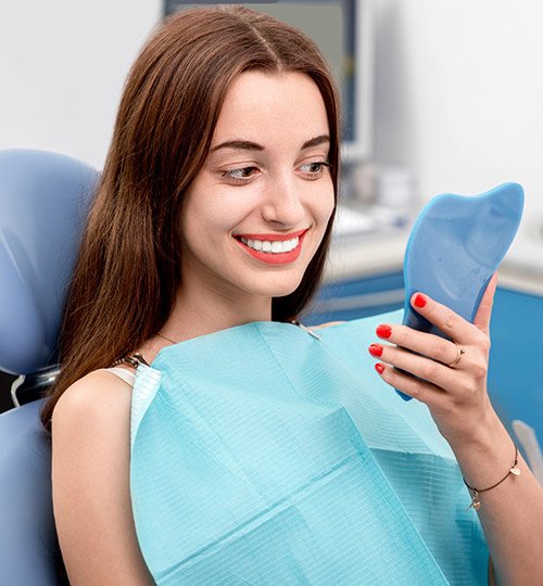 Young woman in dental chair examining smile in mirror