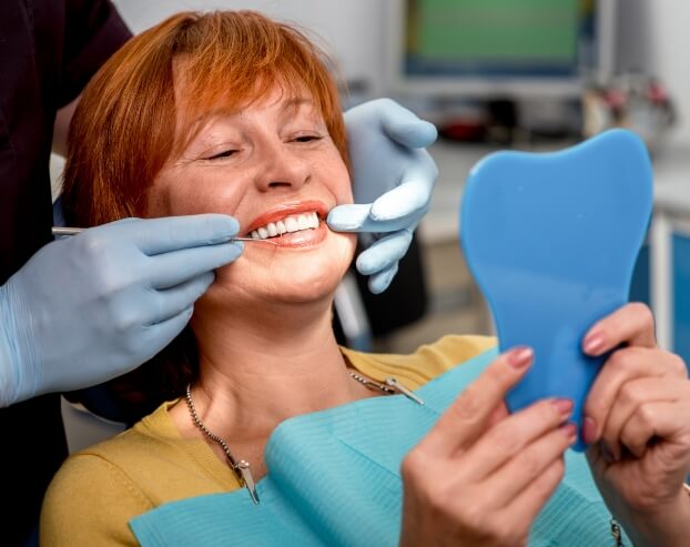 Woman looking at smile after tooth replacement with dental implants