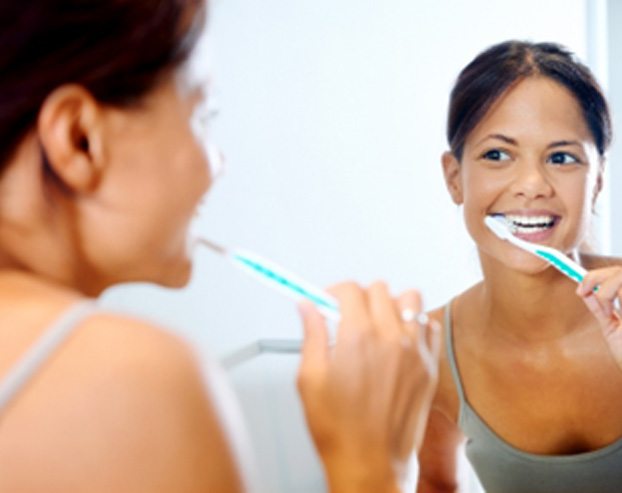 Woman smiling in mirror while brushing her teeth
