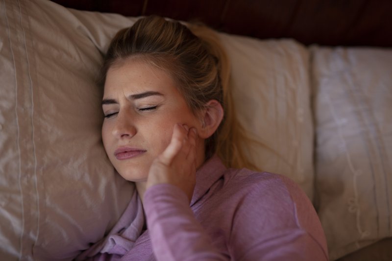 Young woman lying on bed with TMJ headache