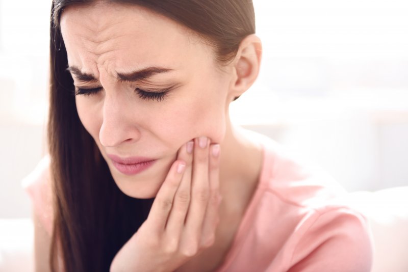 a young woman holding her jaw and cringing in pain because she needs TMJ Therapy in downtown Boston