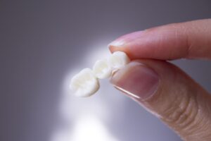 Close up of someone holding a dental bridge between their thumb and forefinger